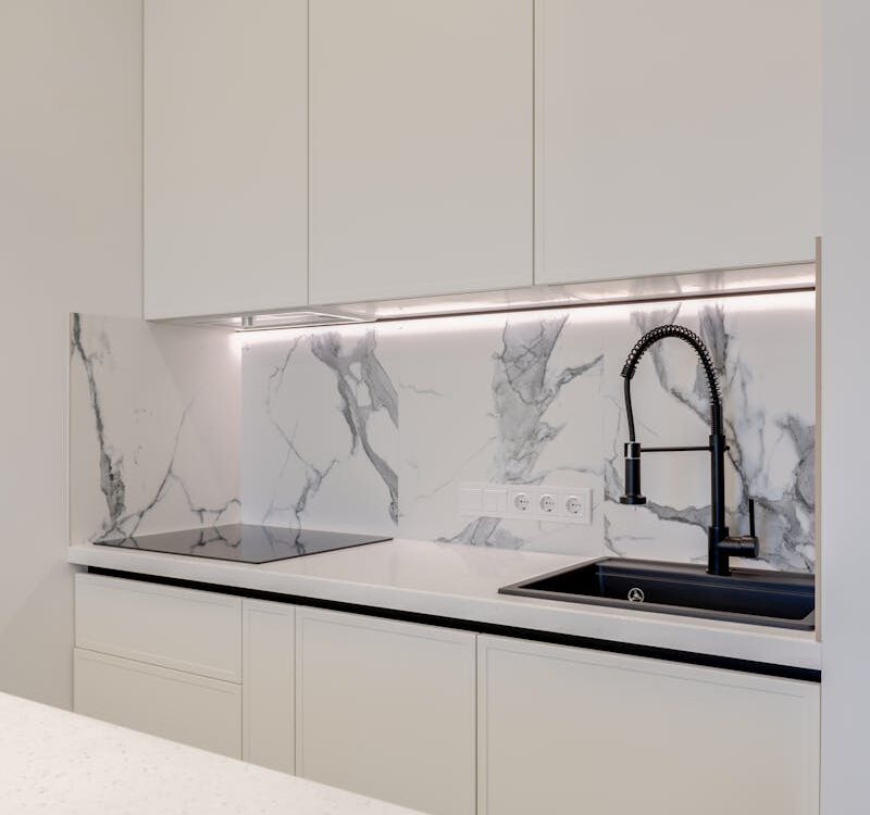 Elegant kitchen featuring white cabinets, marble backsplash, and a black sink.
